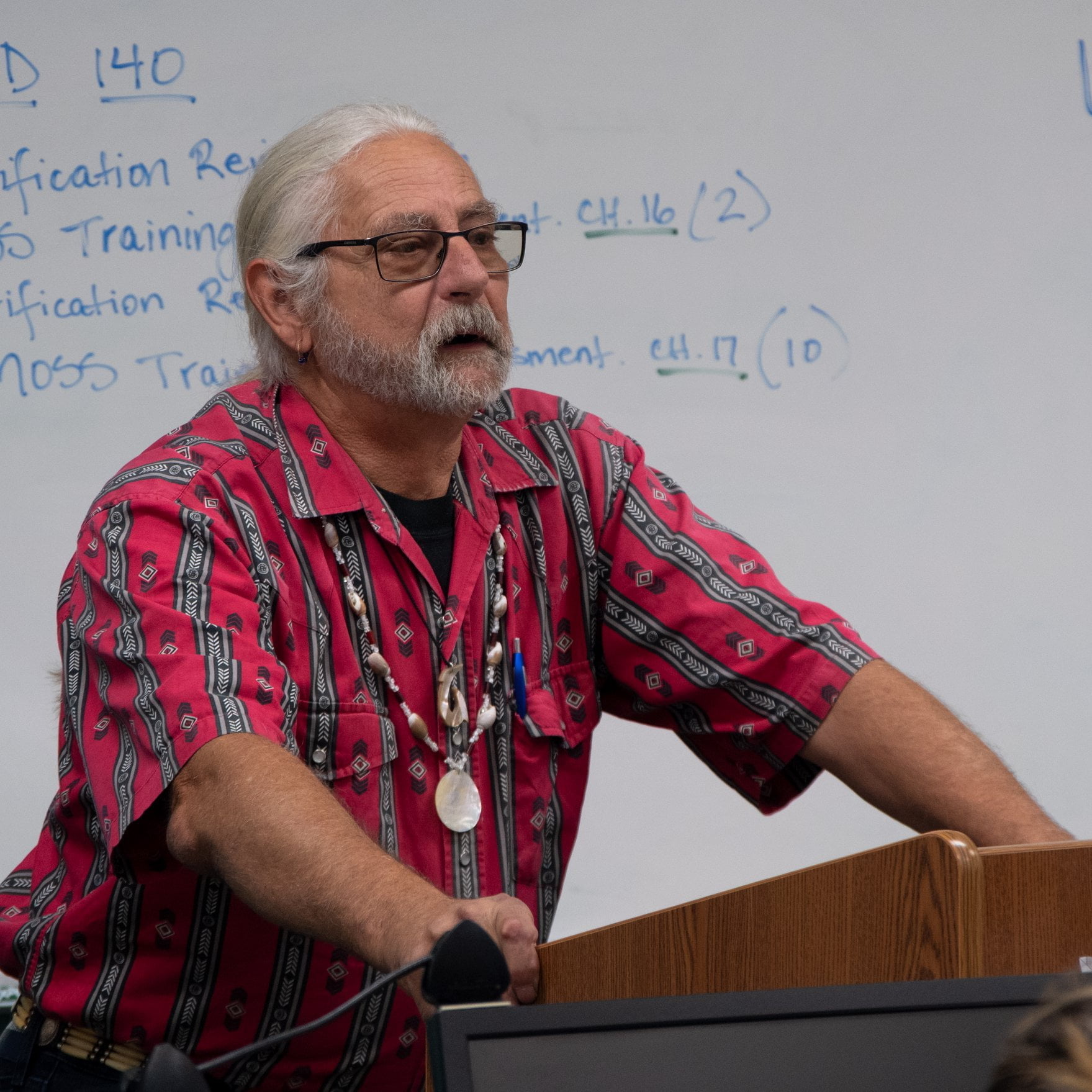 man in red shirt speaking in front of white board