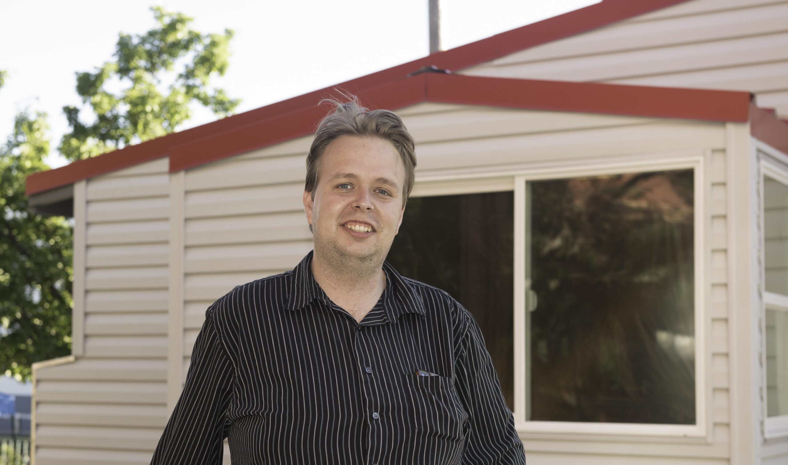 Portrait of Justin Babb next to Shasta Humanity Project's tiny home.